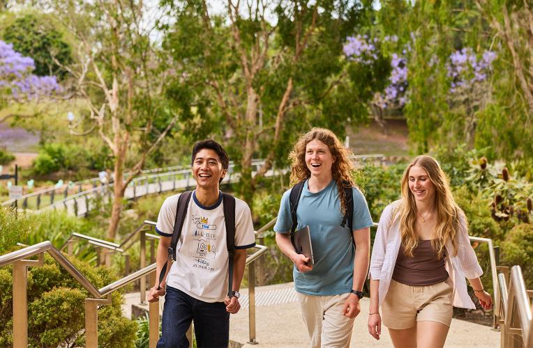 3 students walking through the greenery around the UQ Lakes area.