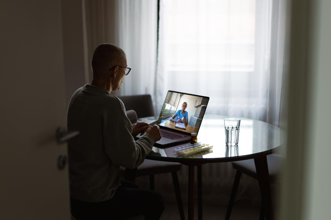 A female oncology patient sitting at her kitchen table having video call with a doctor.