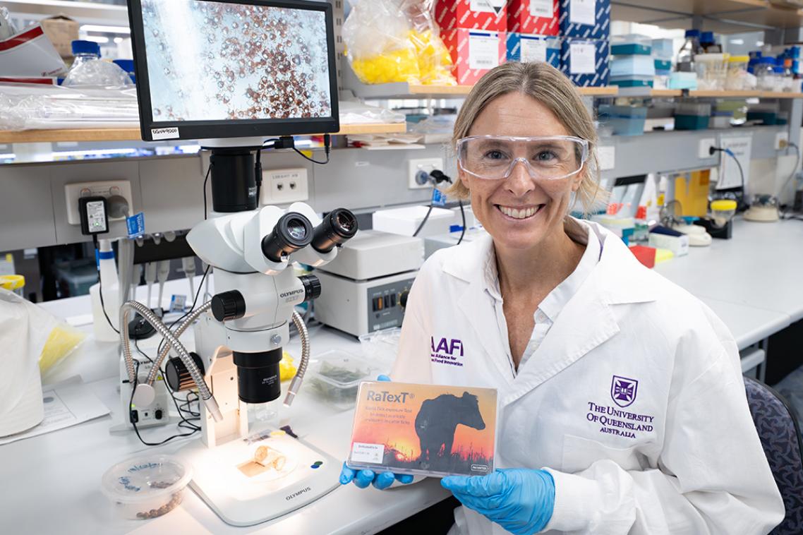 Woman in a science lab wearing protective equipment holds a kit while smiling at the camera