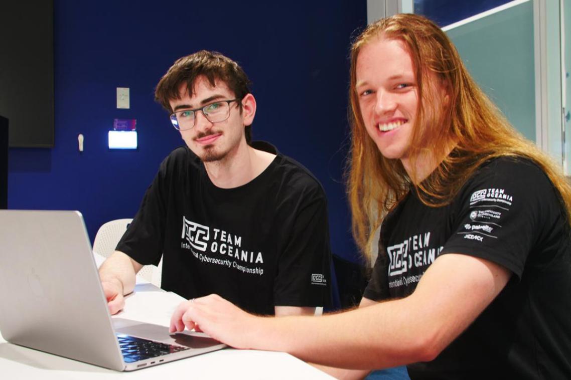 Two male UQ cybersecurity students working in front of a laptop.