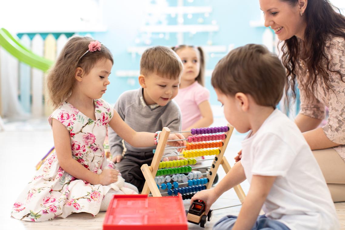 A female educator playing with toddlers wityh toys on the floor in a daycare centre.
