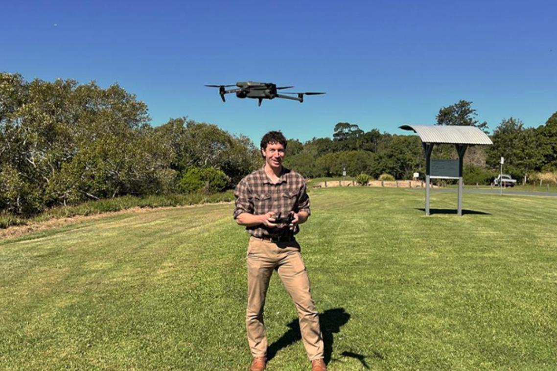 A man standing in a field contolling a drone with a remote control.