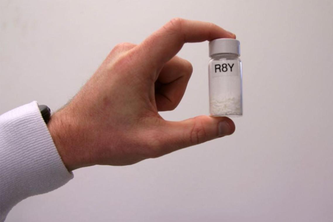 Man's hand holding a drug vial labelled R8Y up to the camera.