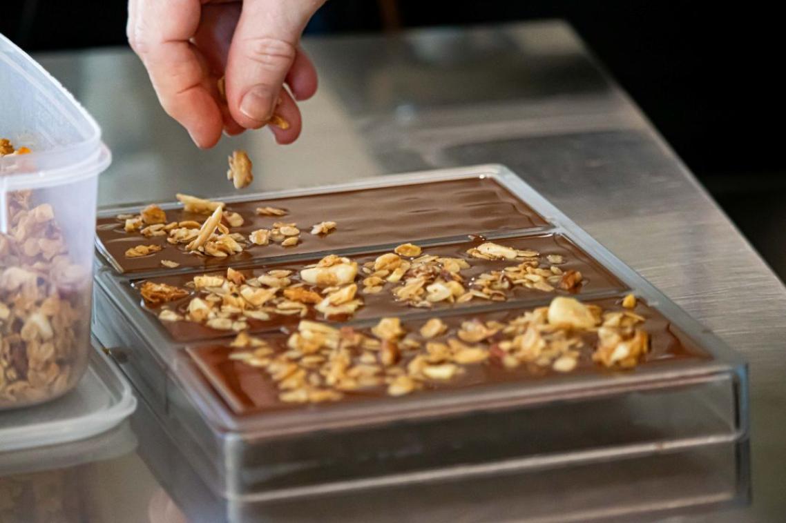 A hand sprinkles nuts over a rectangle of partially melted chocolate  